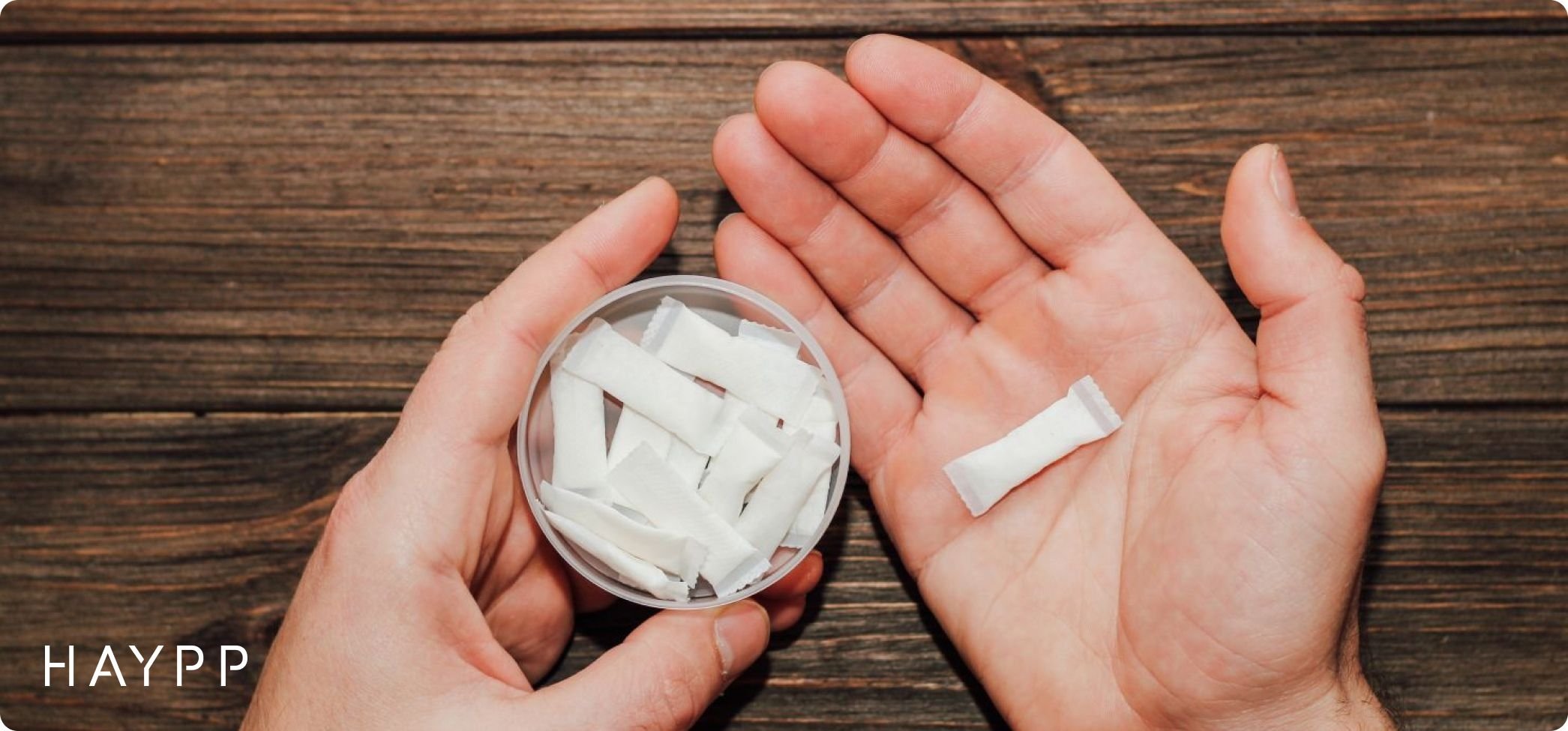 A pair of hands, one holds a nicotine pouch can, the other holds a nicotine pouch